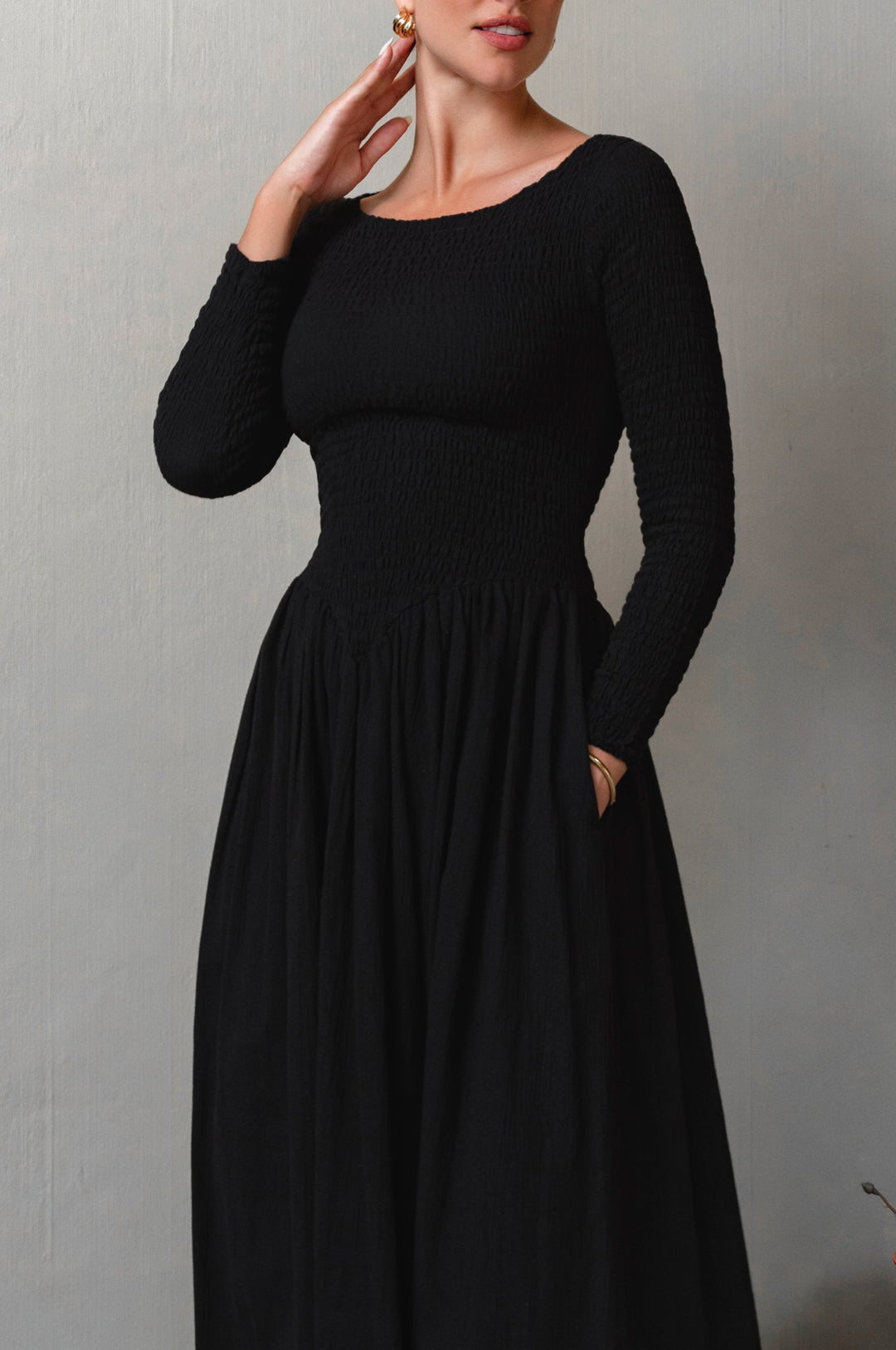 Woman wearing a black long-sleeve smocked dress against a plain background