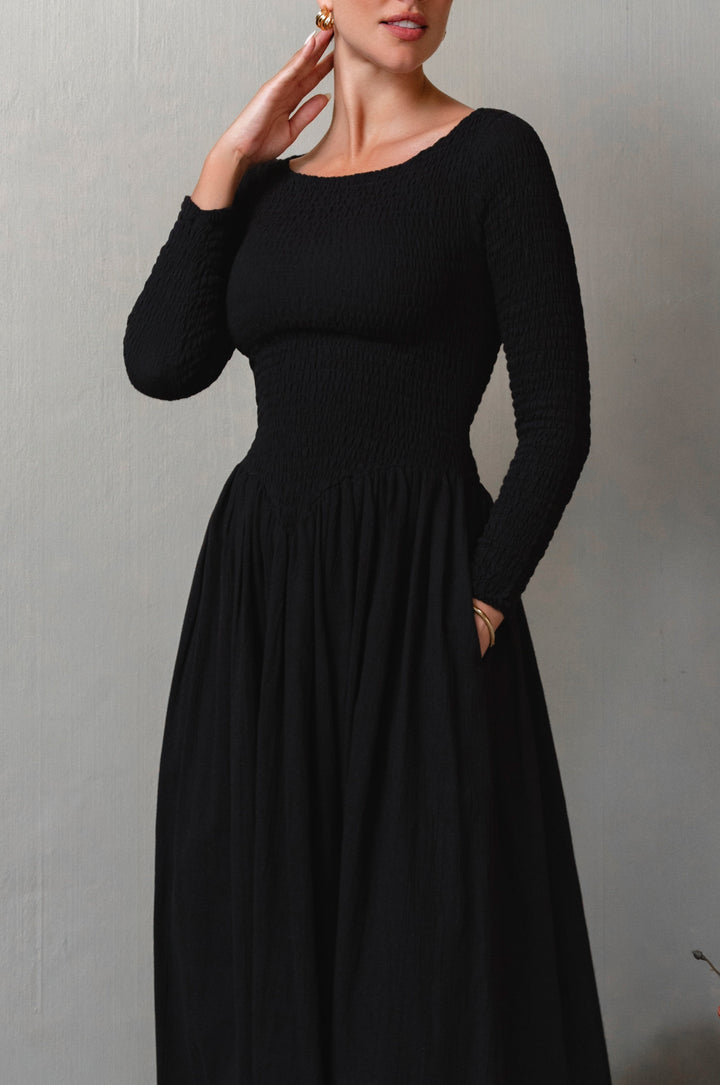 Woman wearing a black long-sleeve smocked dress against a plain background