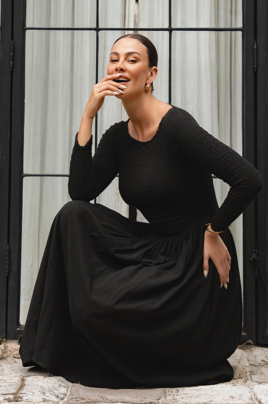 Woman wearing a black linen dress sitting on a stone step.