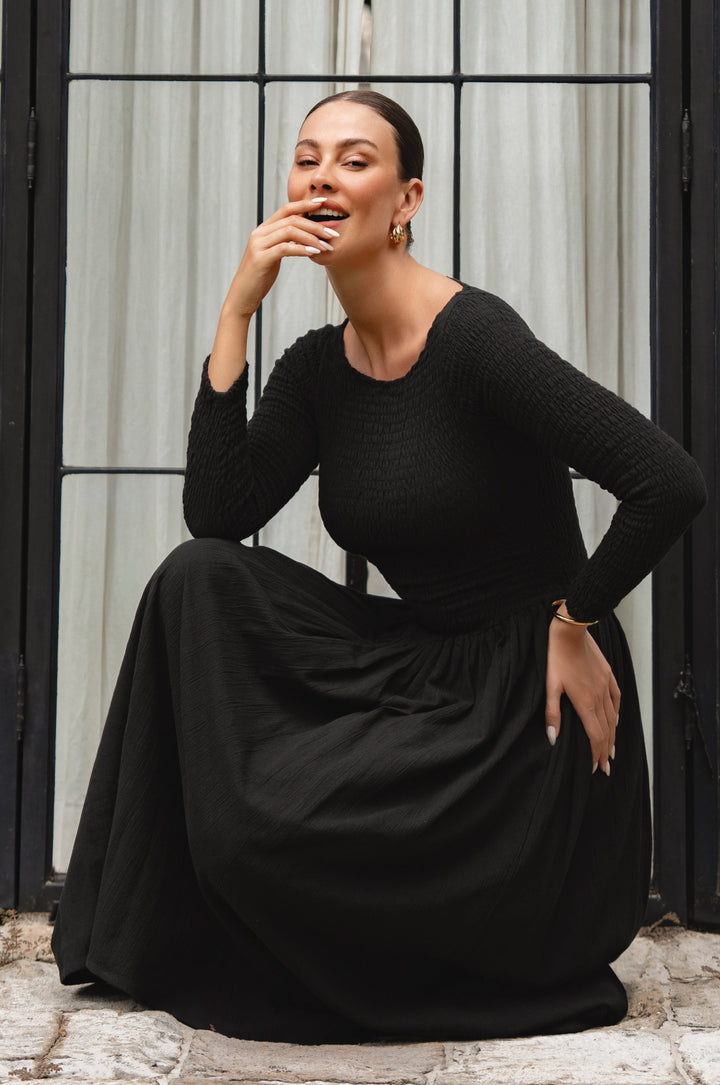 Woman wearing a black linen dress sitting on a stone step.