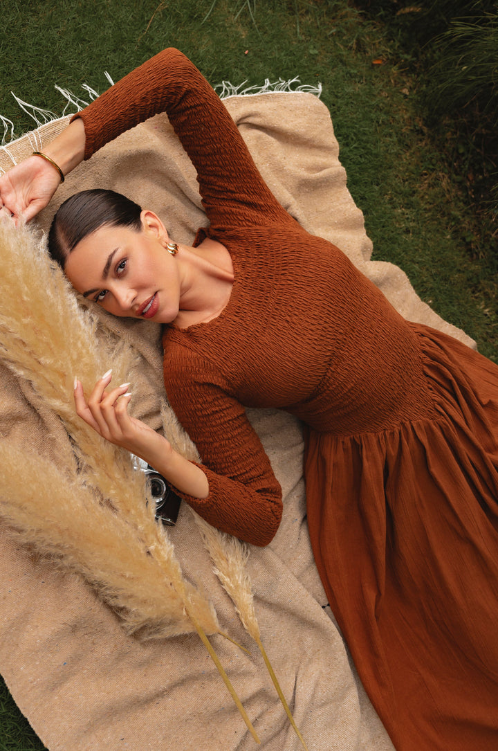 Woman in a brown dress lying on a blanket with pampas grass
