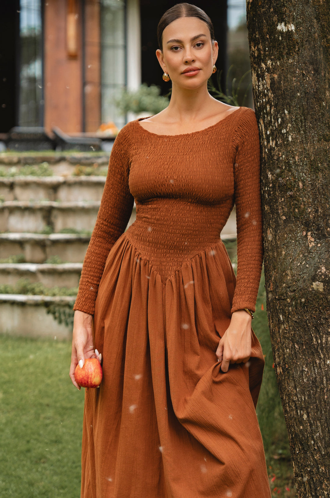 Woman in a rust-colored midi dress standing next to a tree outdoors.