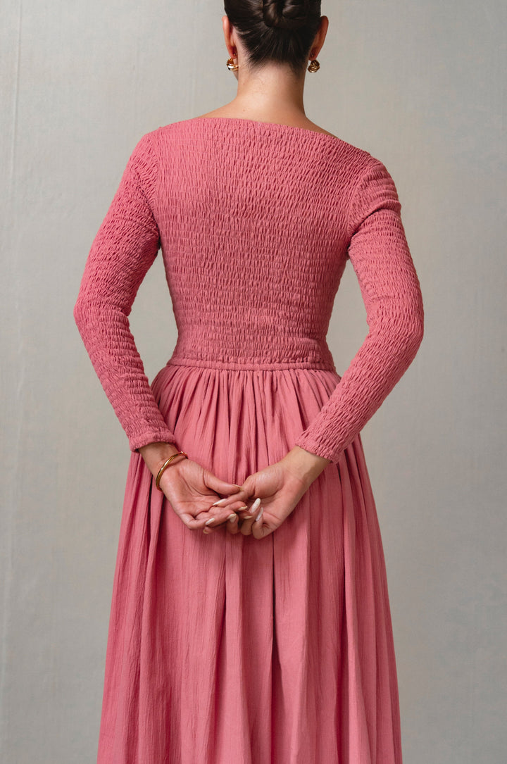 Person wearing a pink smocked dress against a plain background