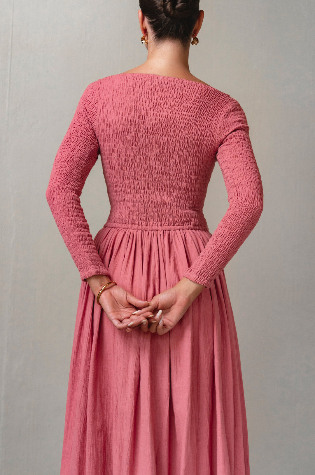 Person wearing a pink smocked dress against a plain background