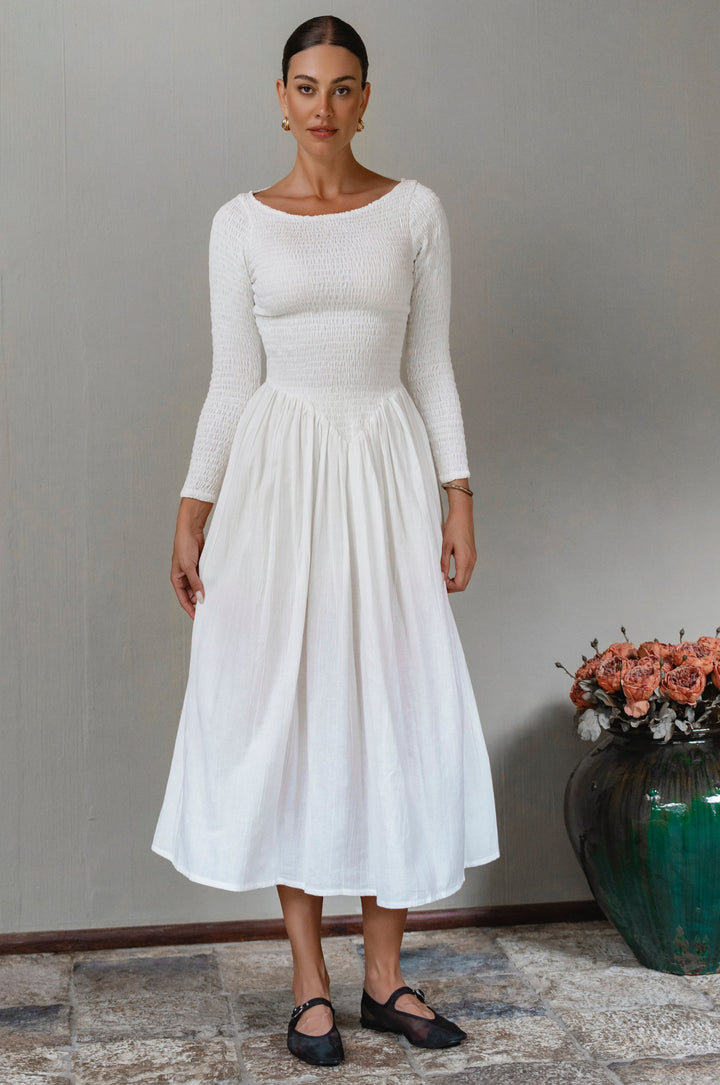 Woman wearing a white smocked long sleeve midi dress standing against a plain background
