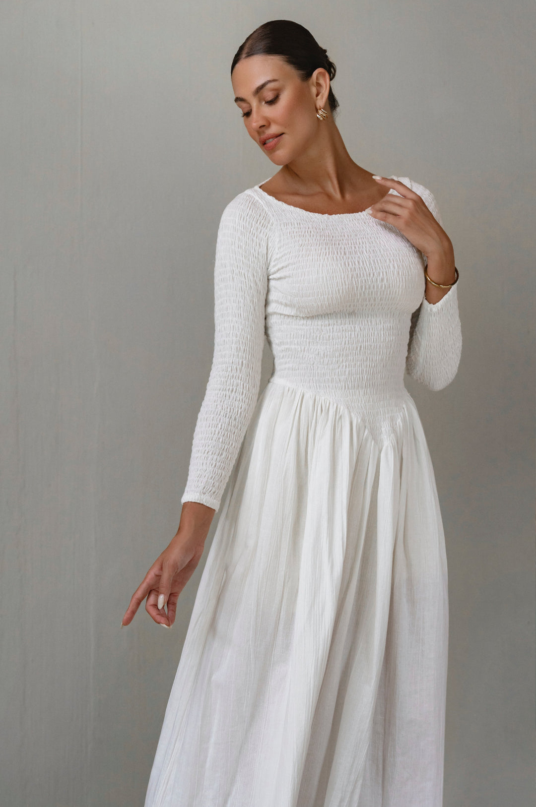 Woman wearing a white long-sleeve linen dress against a gray background