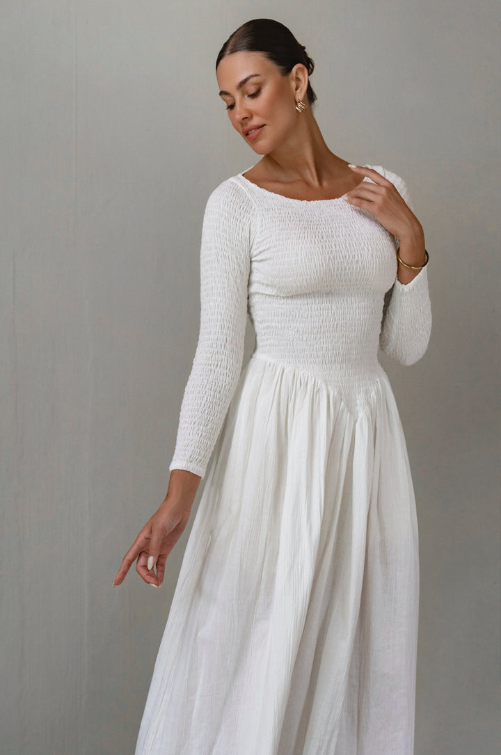 Woman wearing a white long-sleeve linen dress against a gray background