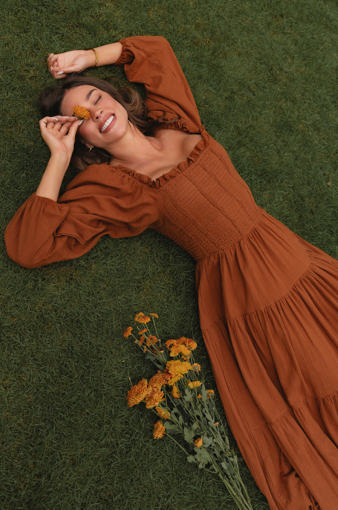 Woman in a brown midi dress lying on grass with flowers nearby country style 