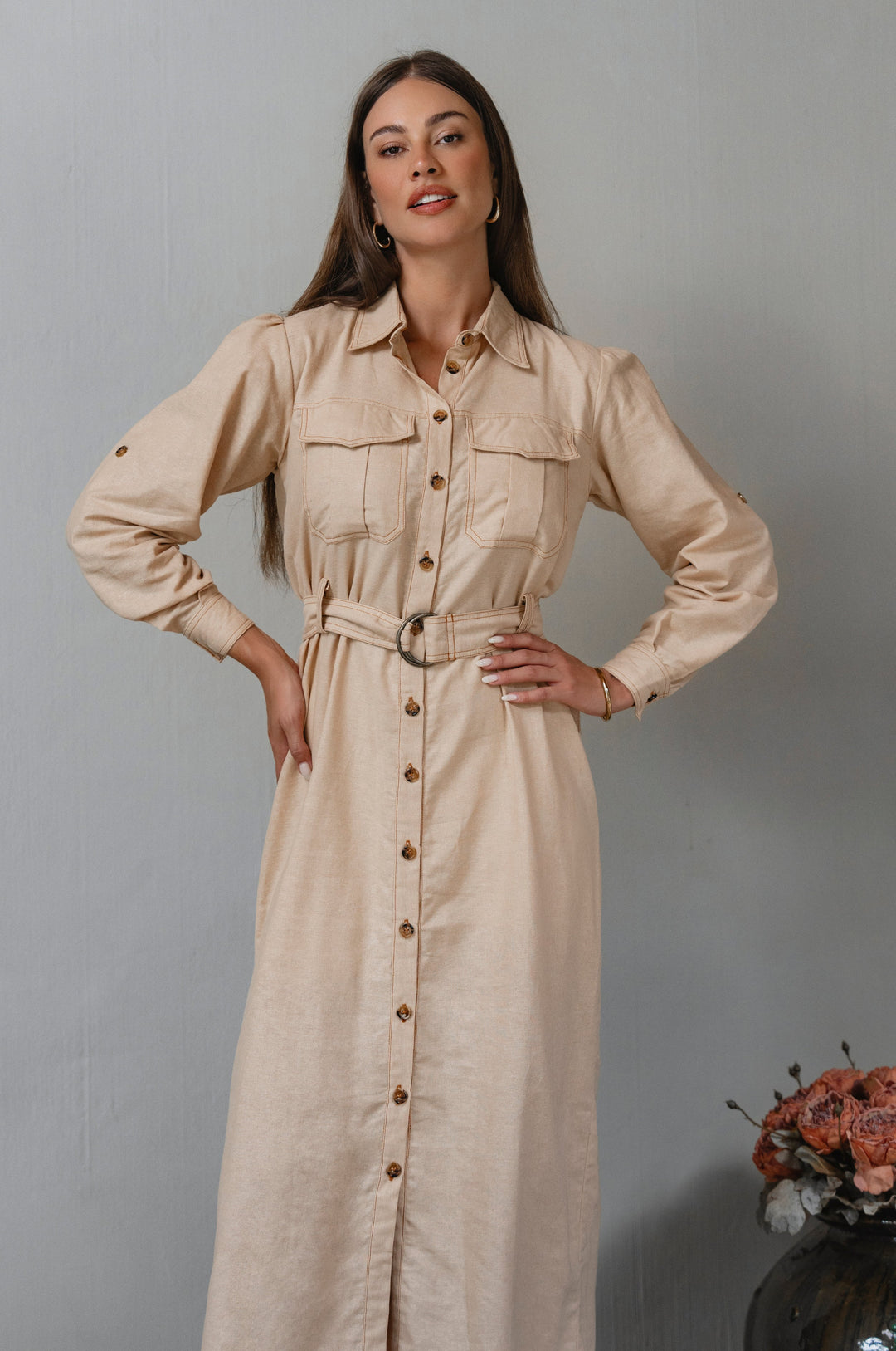 Woman wearing a beige dress with a belt against a gray background