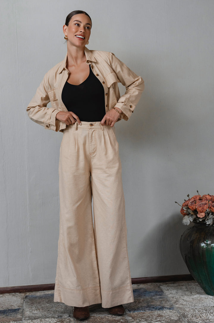 Woman wearing a beige jacket and pants with a black top, standing against a plain wall -cottage core style