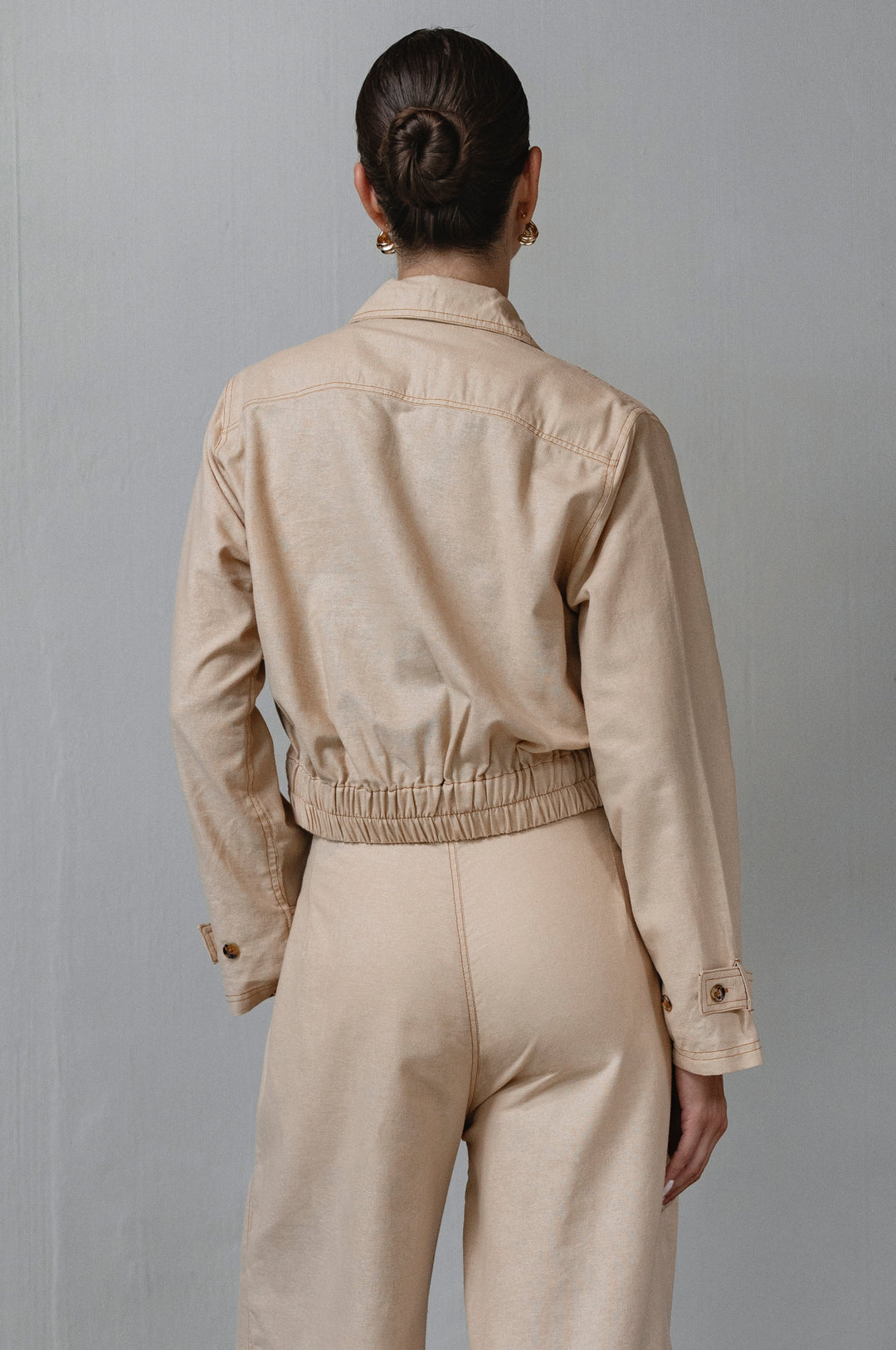 Person wearing a beige jacket and pants against a gray background