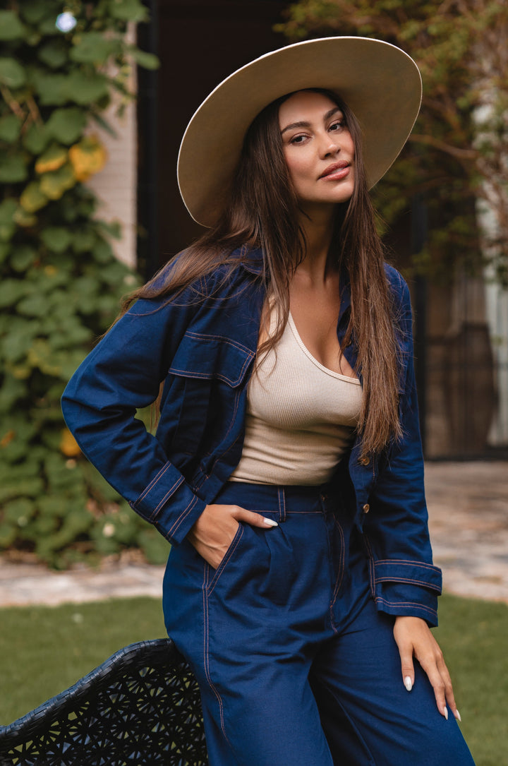 Woman wearing a blue denim outfit with a beige hat in an outdoor setting