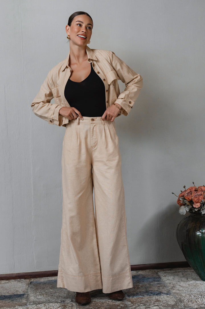 Woman wearing a beige jacket and pants with a black top, standing against a plain wall. - cottage core style