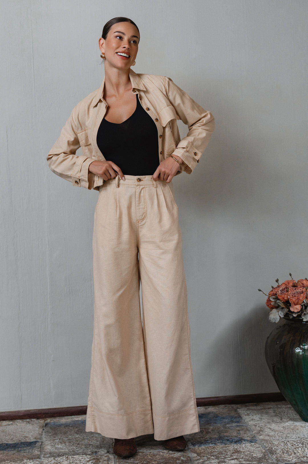 Woman wearing a beige jacket and pants with a black top, standing against a plain wall. - cottage core style
