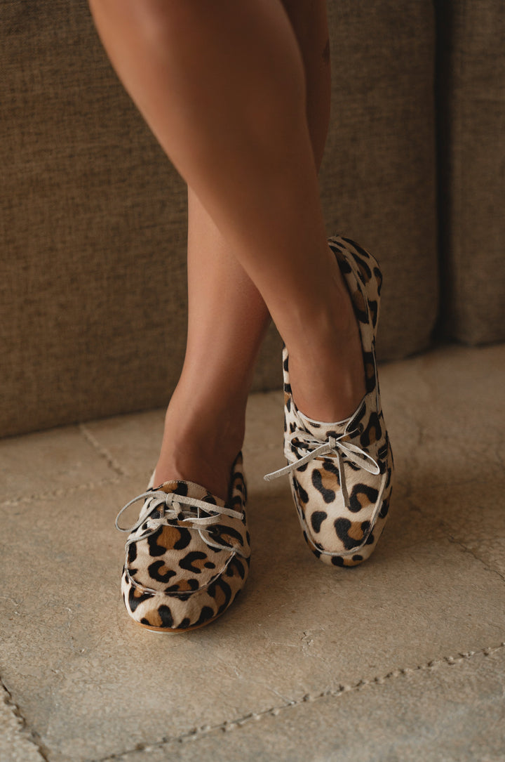 Leopard print shoes worn by a person on a stone floor with a neutral background