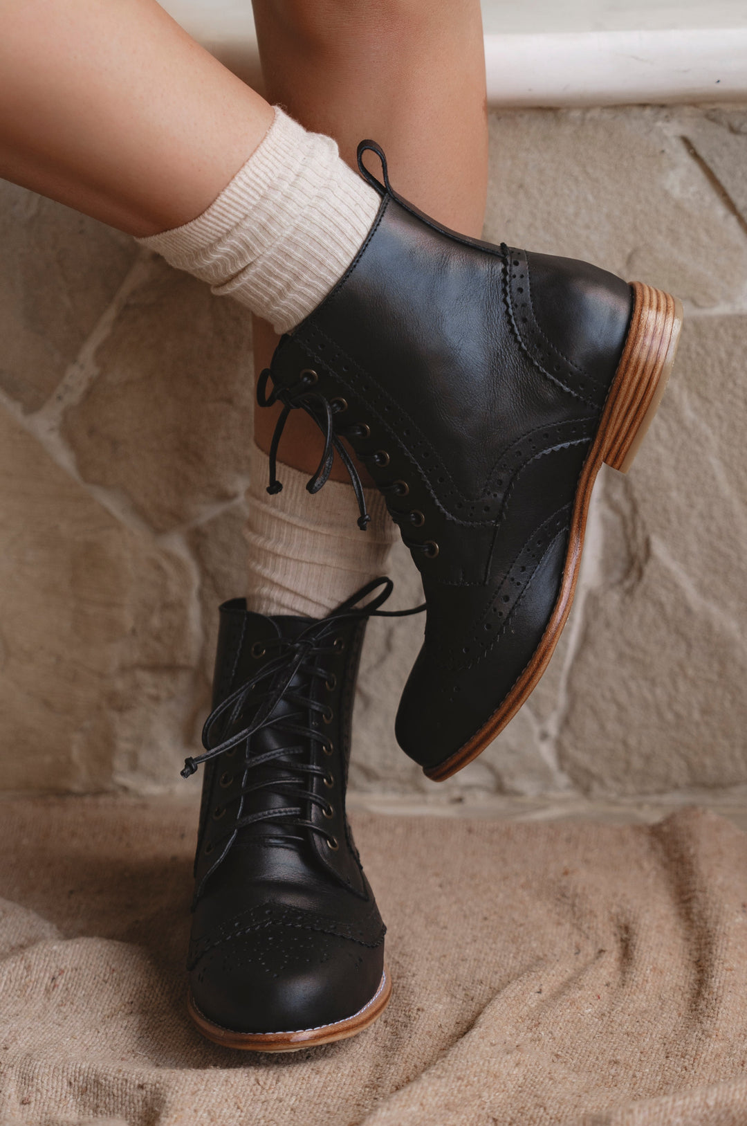 Black leather boots with brown soles worn indoors on a stone floor.