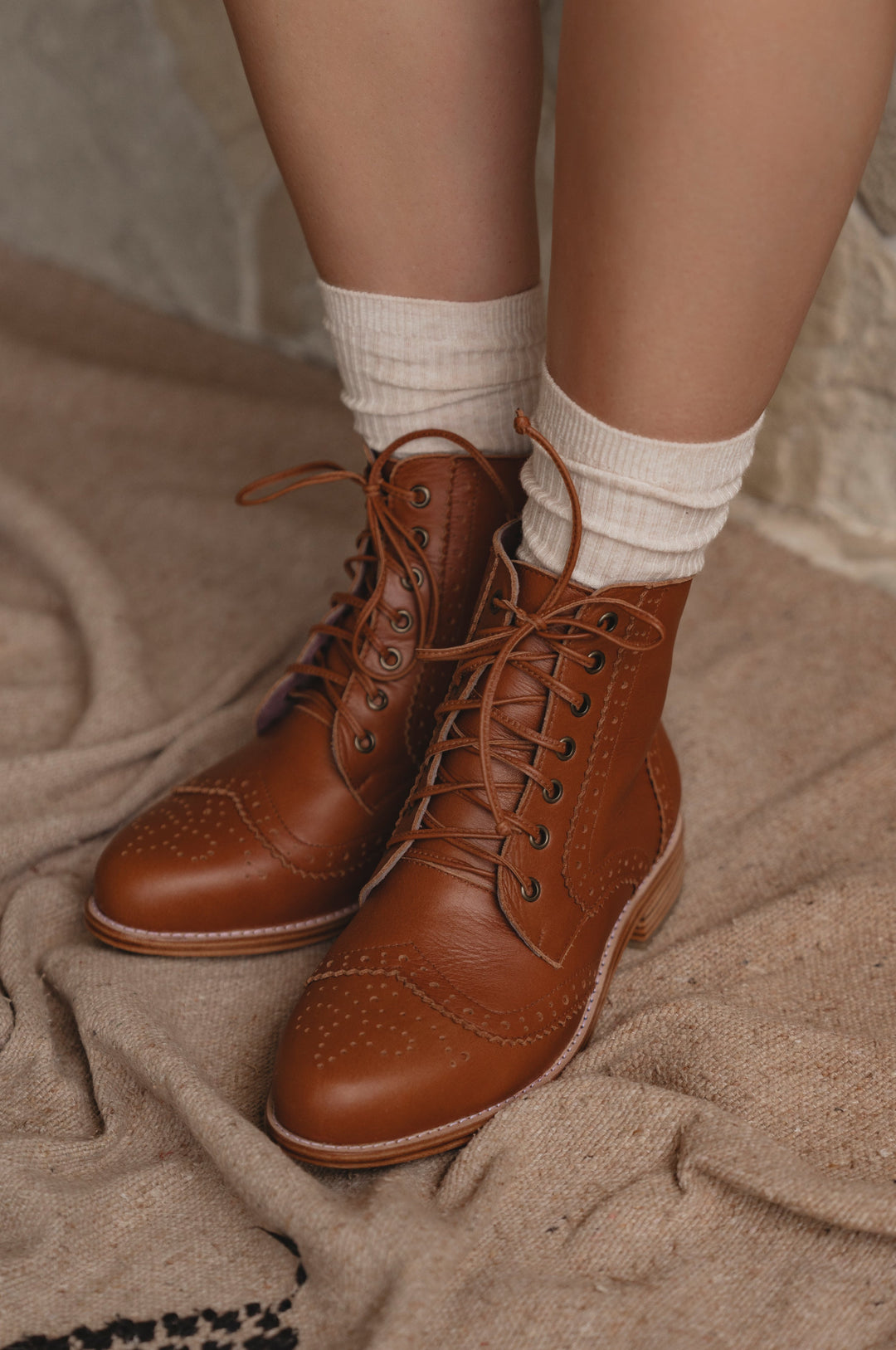 Brown lace-up boots worn with white socks on a textured surface
