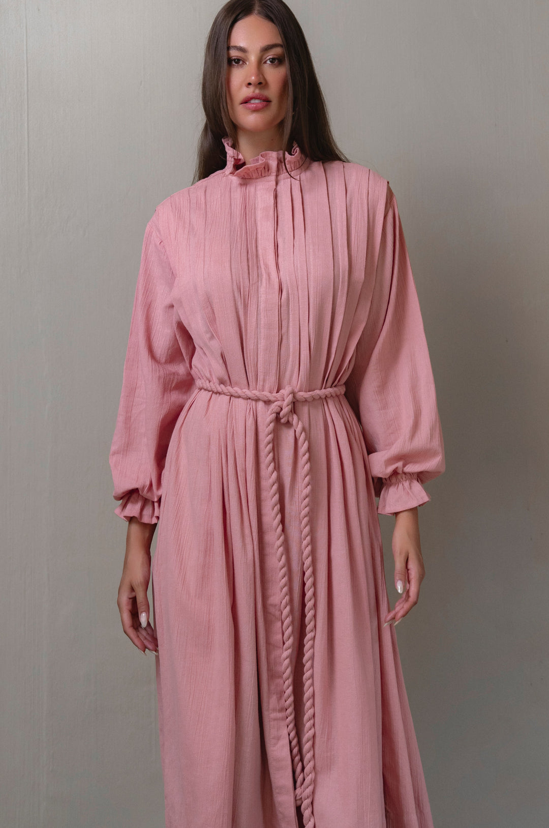 Woman wearing a pink dress with long sleeves against a gray background